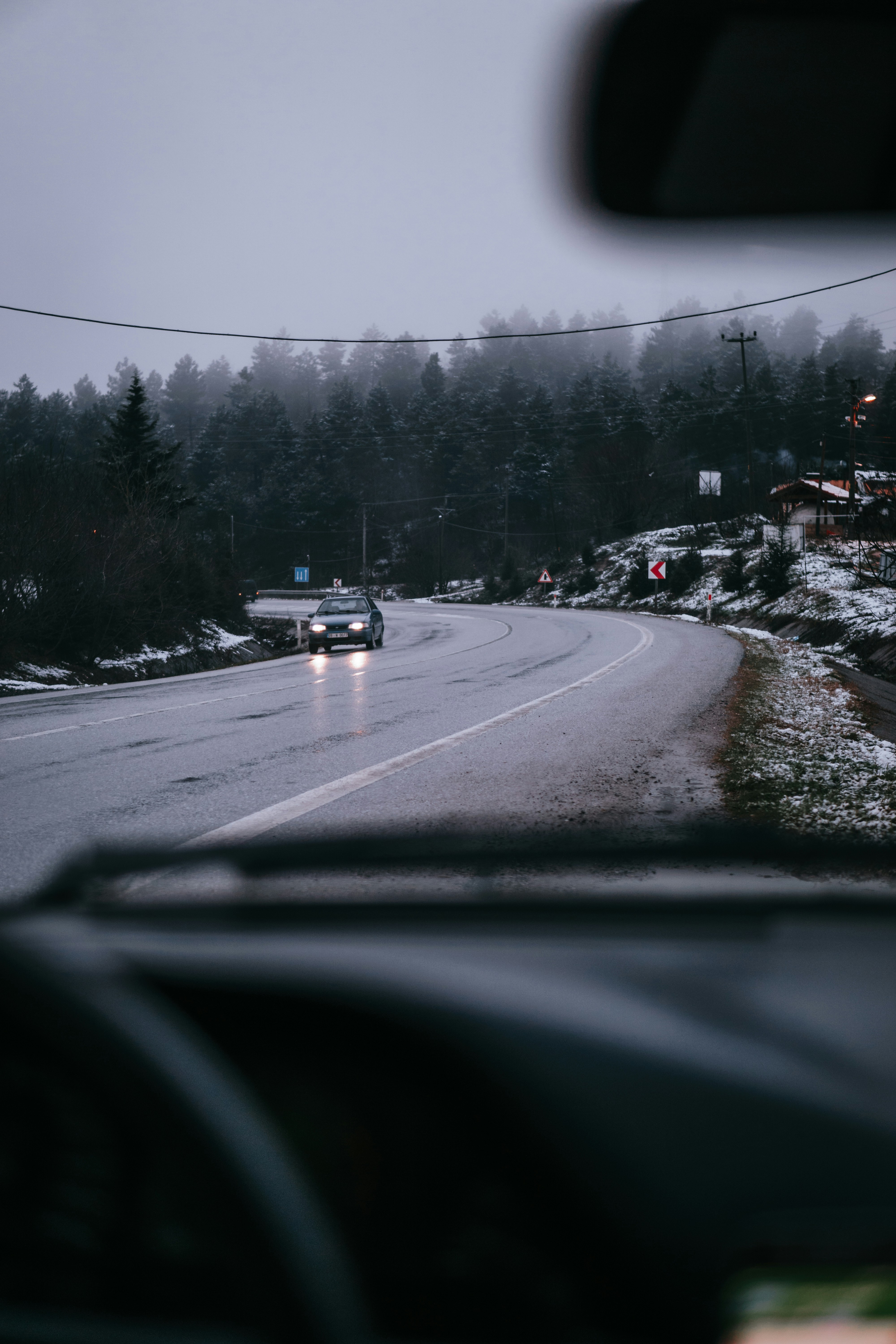 Car driving along a wet curving road in misty winter conditions viewed from inside another vehicle.